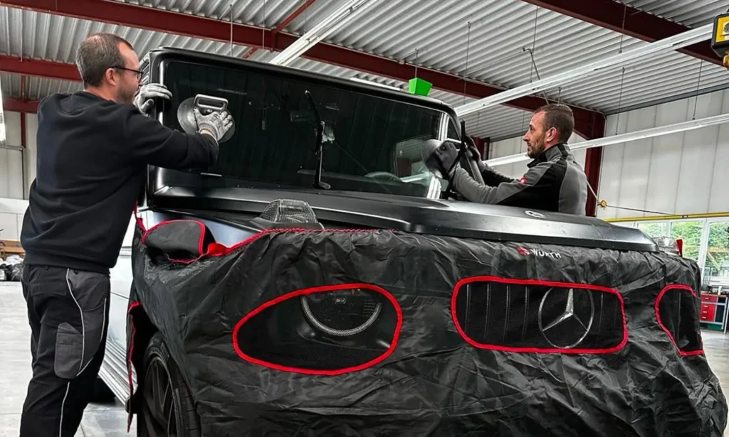 Zwei Autoglas-Techniker setzen eine Windschutzscheibe in eine Mercedes G-Klasse ein